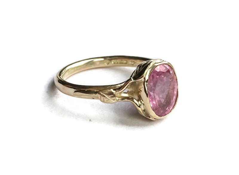 gold ring with leaf and twig details set with large pink gemstone, on white background