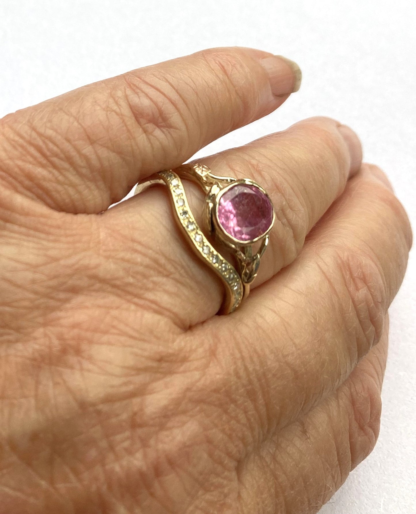 gold cocktail ring with big oval pink stone and diamond set wedding ring, on hand