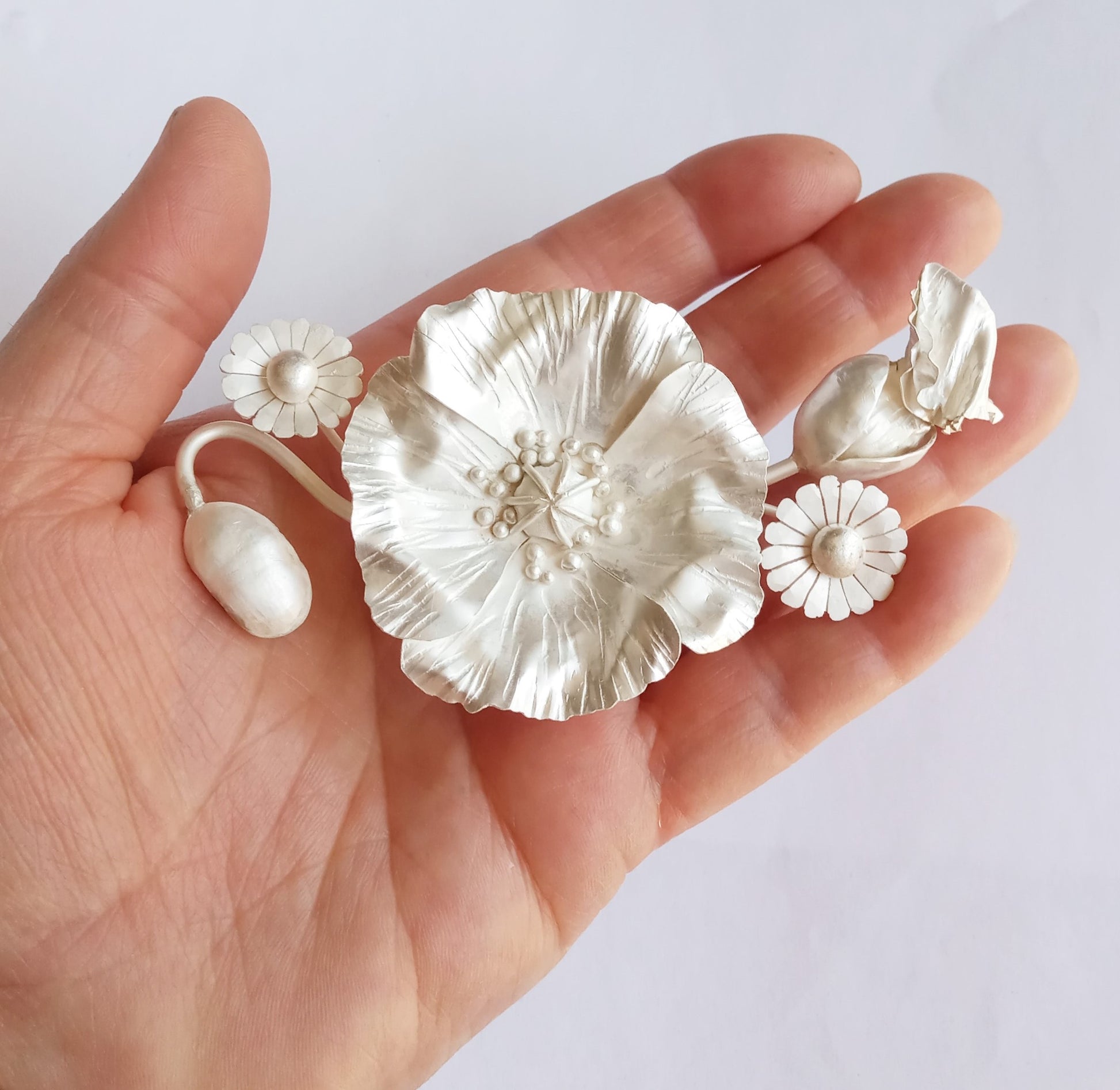 in progress close up of sterling silver hand forged poppy, still white from the acid, held in hand