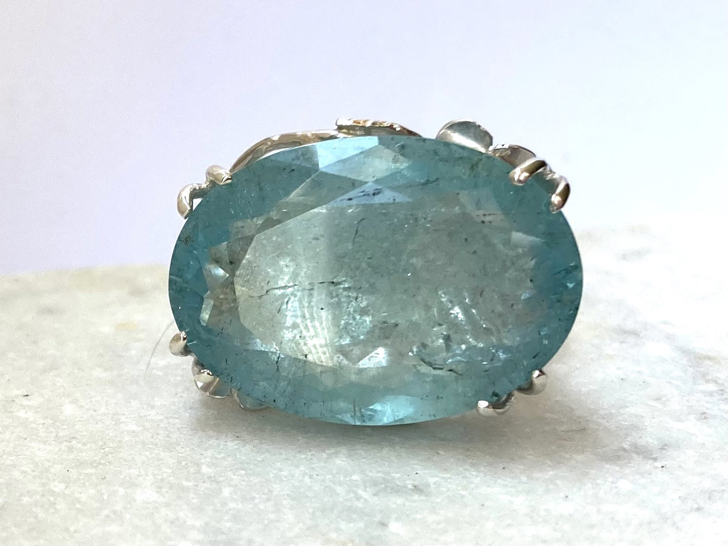 close up of oval aquamarine prong set cocktail ring, on marble background