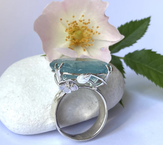 aquamarine floral ring with openwork setting, resting on white pebble with real wild rose