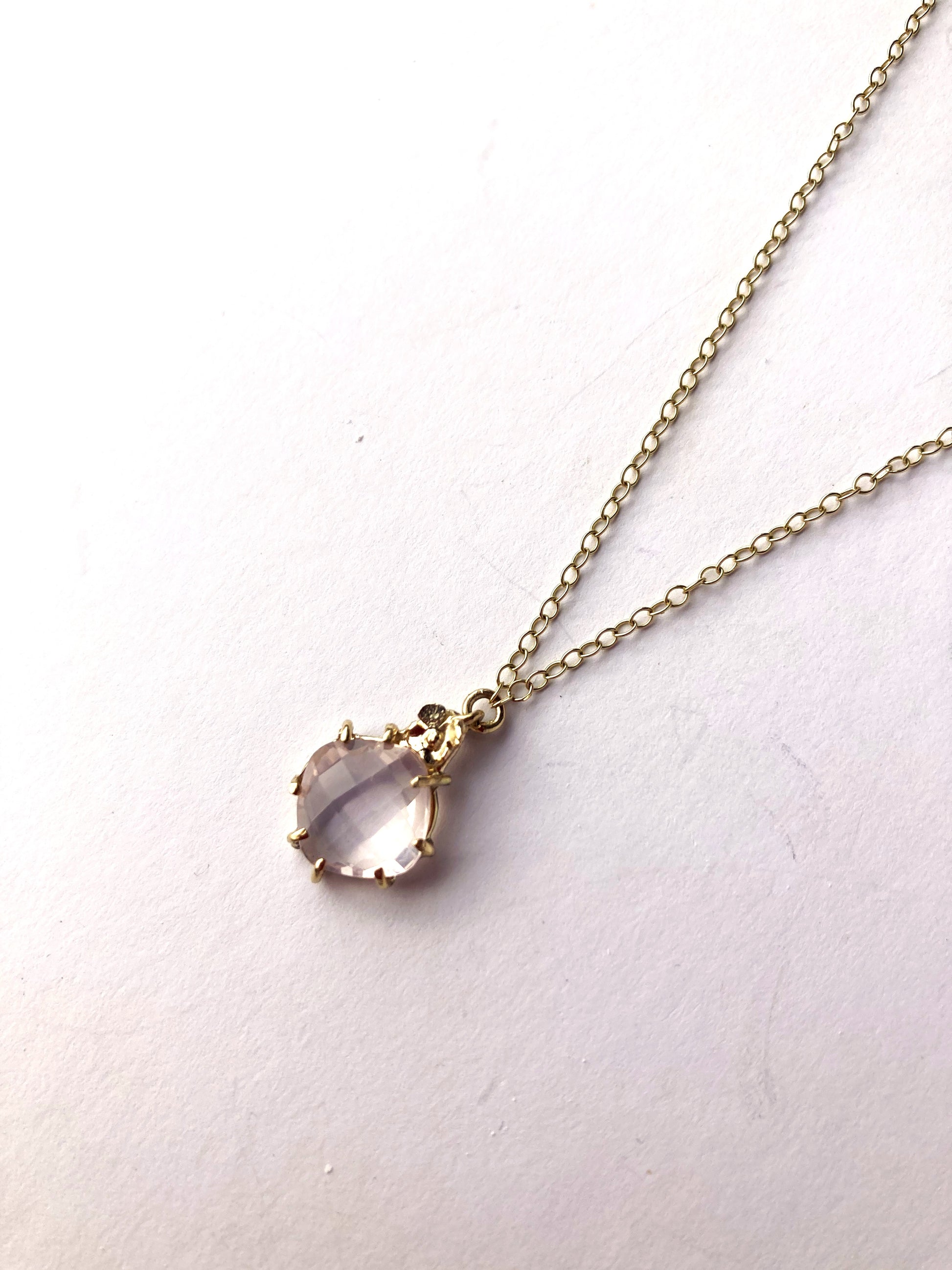 gold pendant and chain with pale pink rose quartz gemstone, on grey background