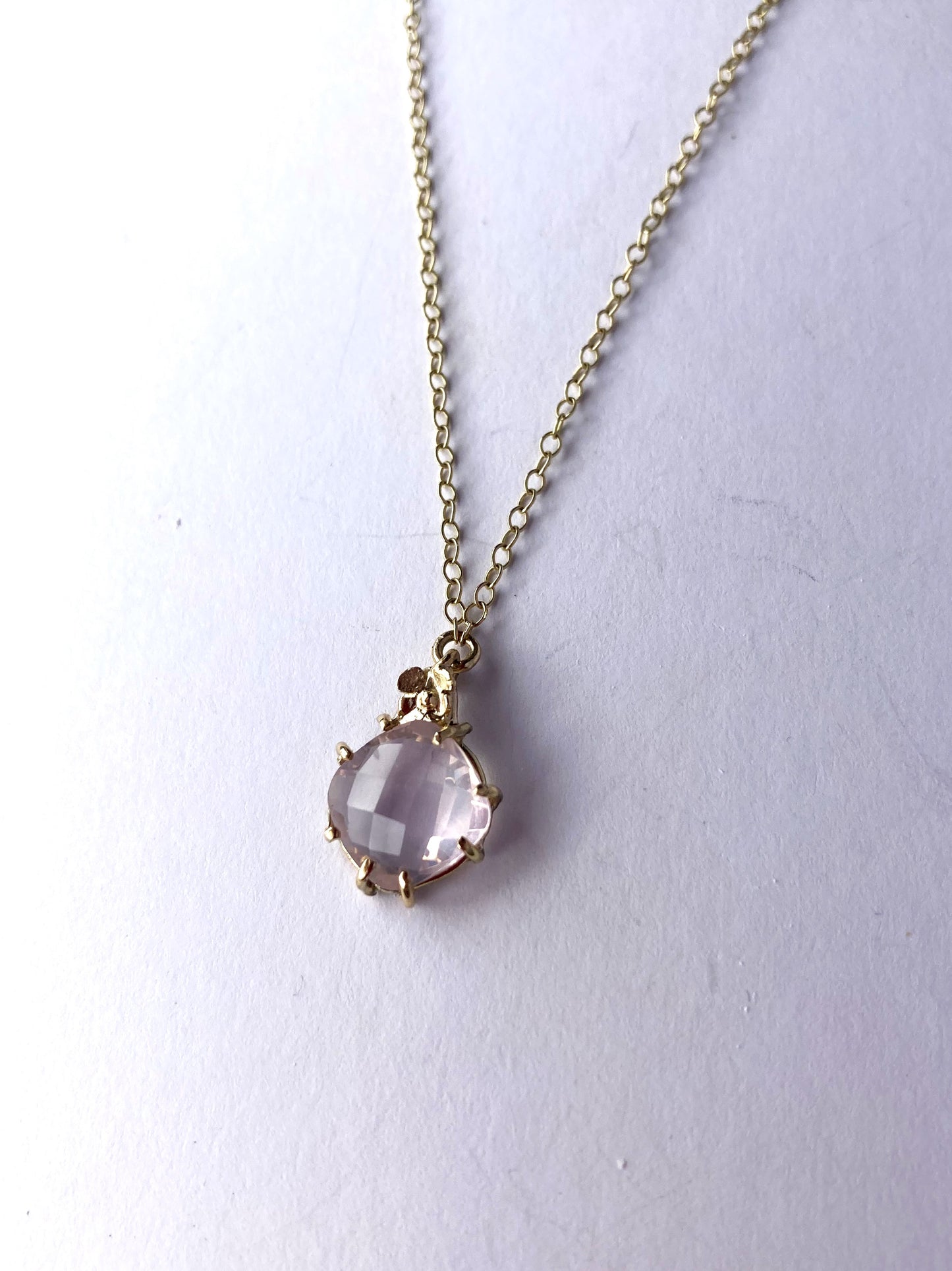 gold and rose quartz prong set pendant and chain on grey background