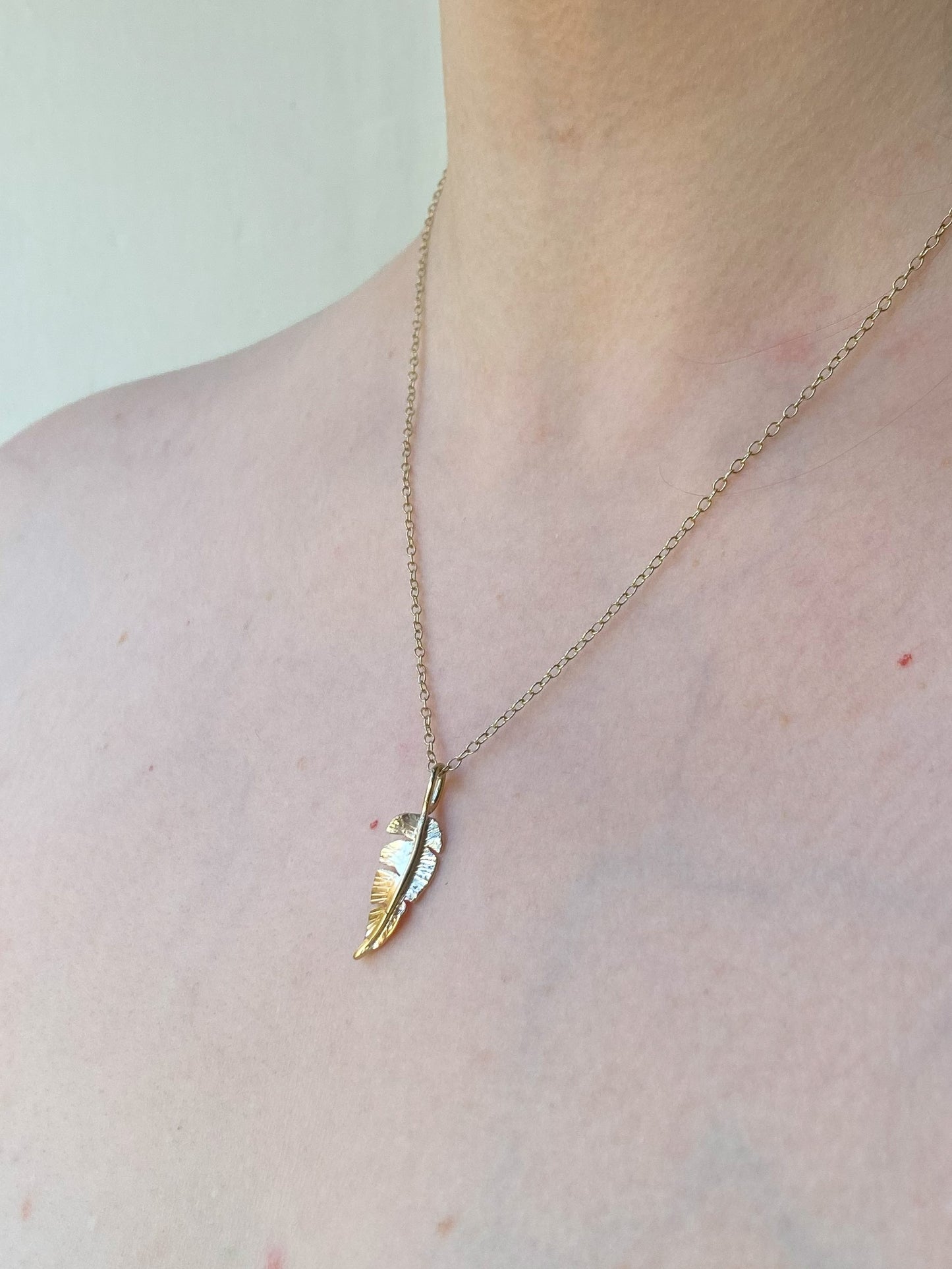 Yellow gold hand forged feather pendant and chain on woman's neck