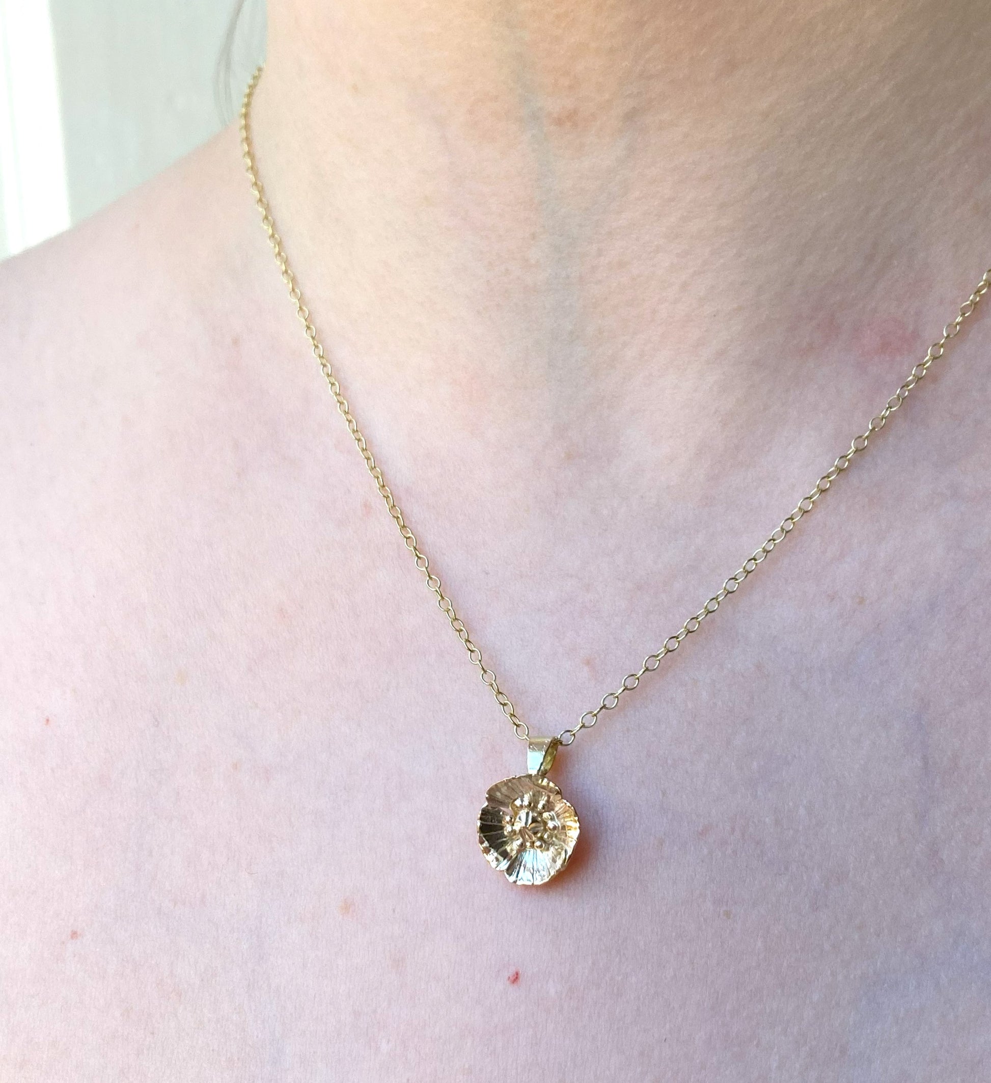 Hand forged yellow gold poppy pendant and chain on woman's neck