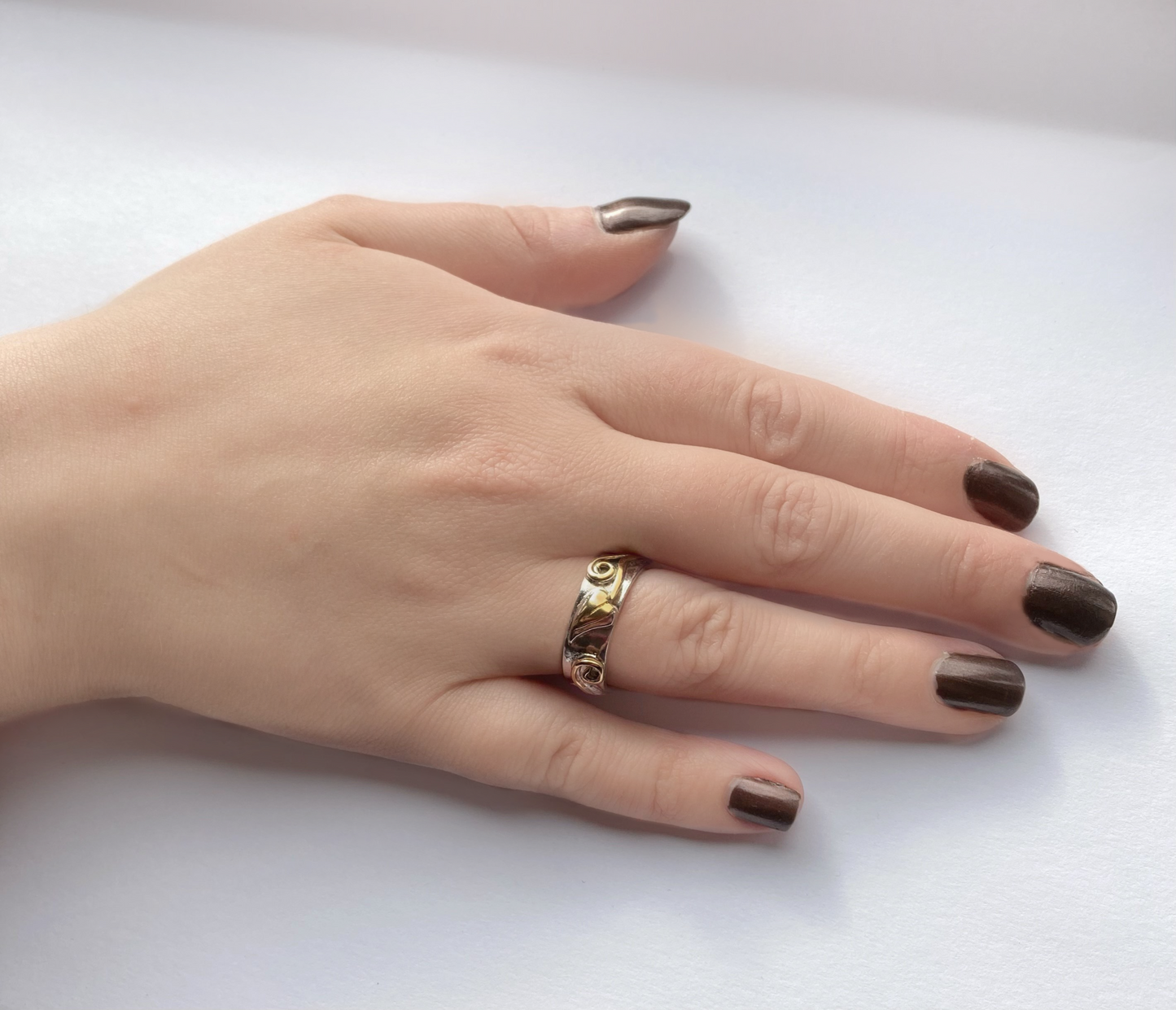 white and yellow gold wedding band with gold leaf and scroll details in relief, shown on hand