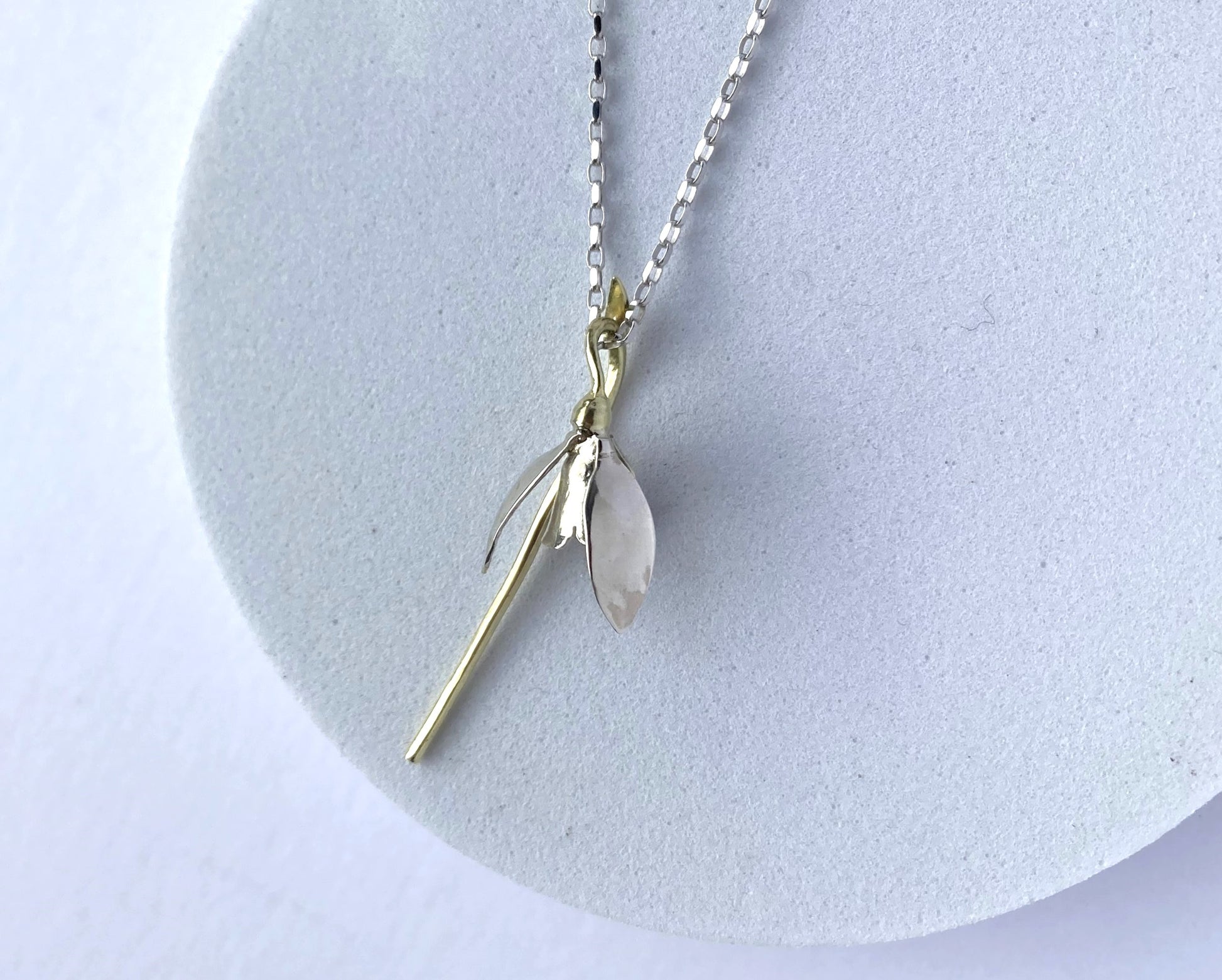 white and green gold hand forged botanic snowdrop pendant on white plinth