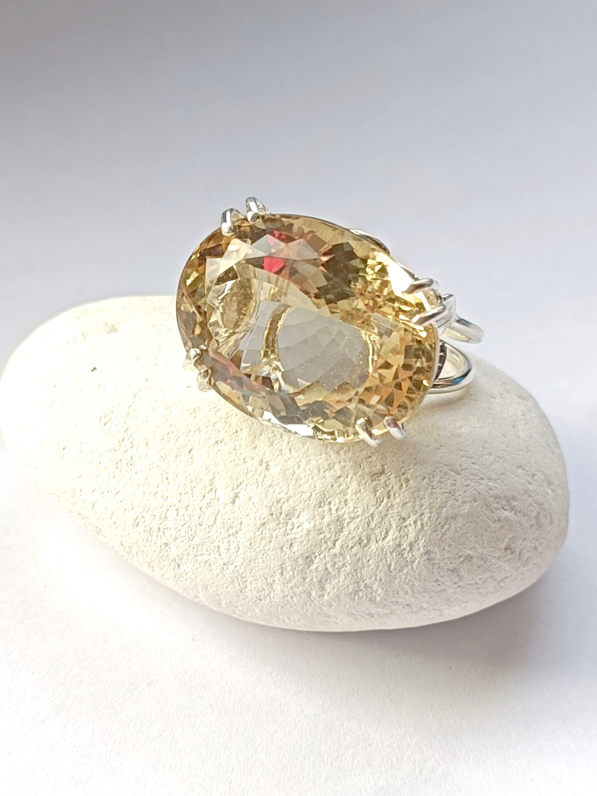 big yellow citrine gemstone cocktail ring resting on white pebble