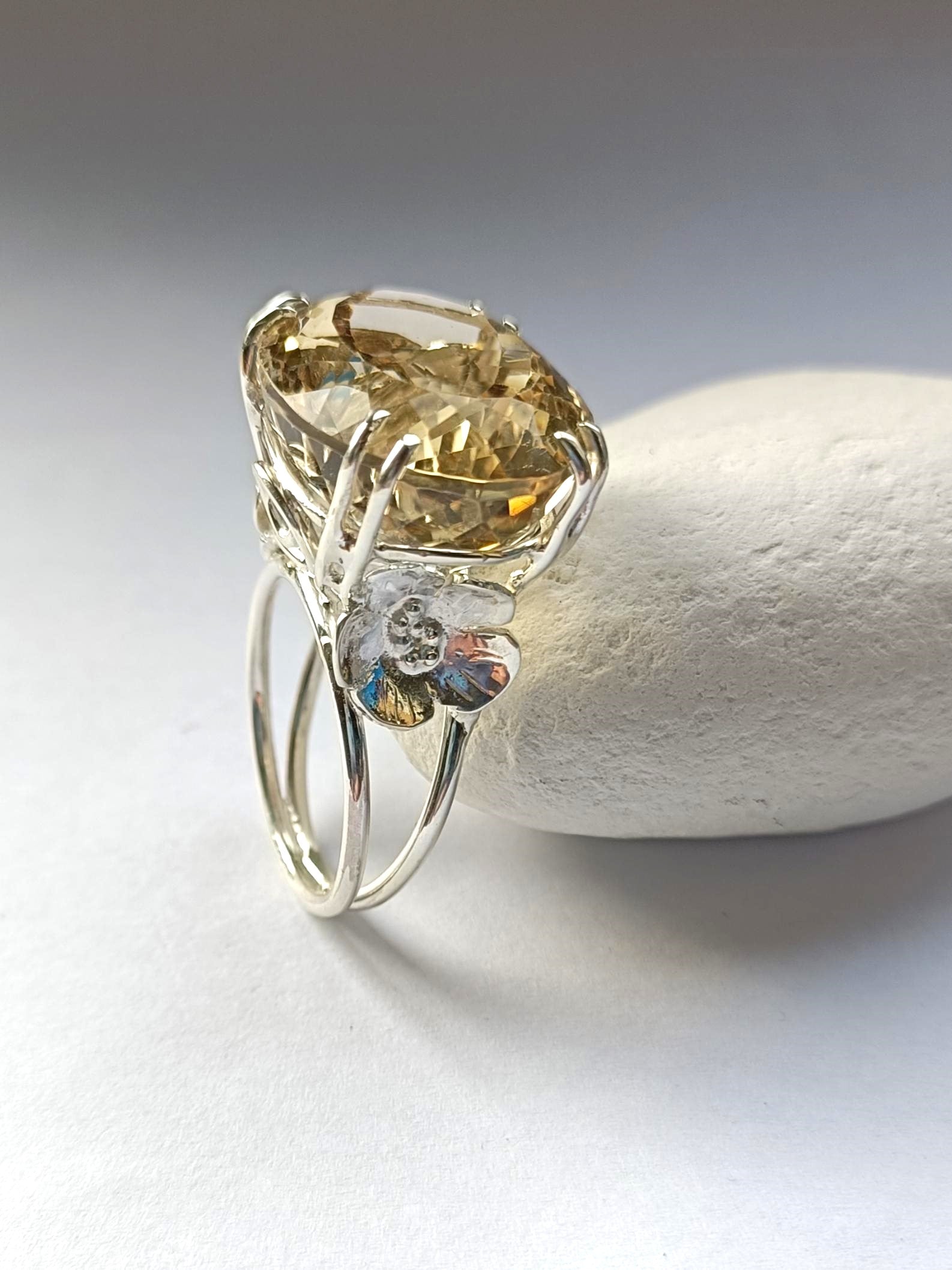 large yellow citrine  prong setting ring with flower details, resting on white pebble