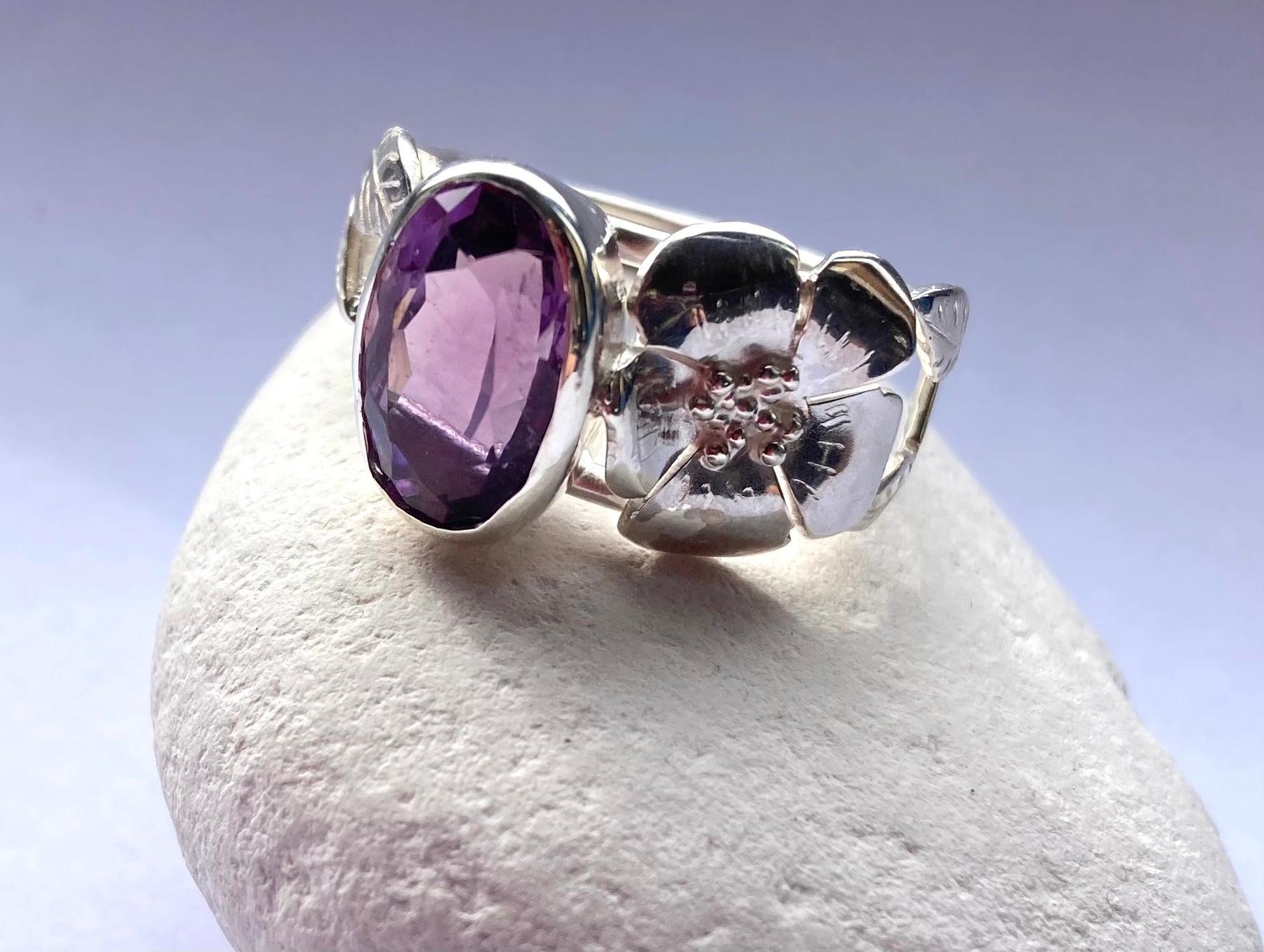 oval purple amethyst and silver rose  ring on white pebble