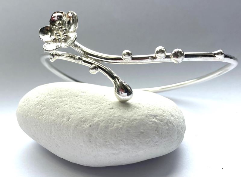 sakura cherry blossom bangle in sterling silver, resting on white pebble