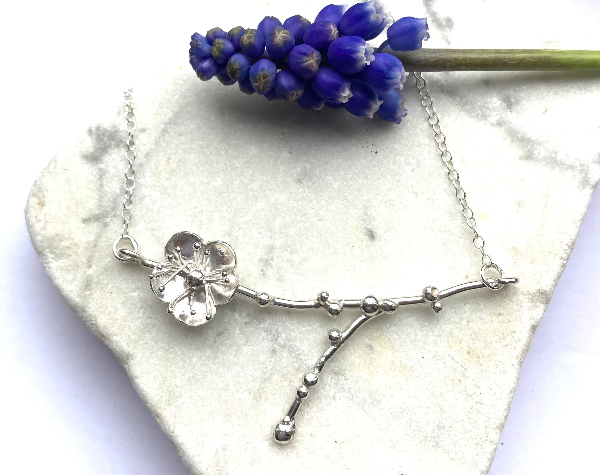 single flower and twig silver necklace, with real muscari, on marble background