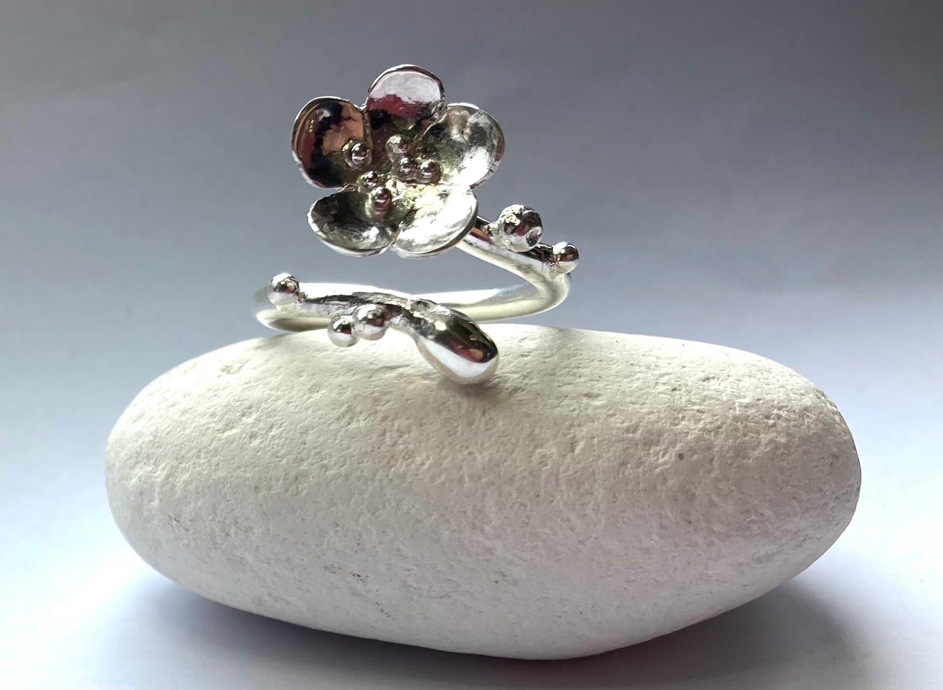 curving hand forged flower ring, on white pebble