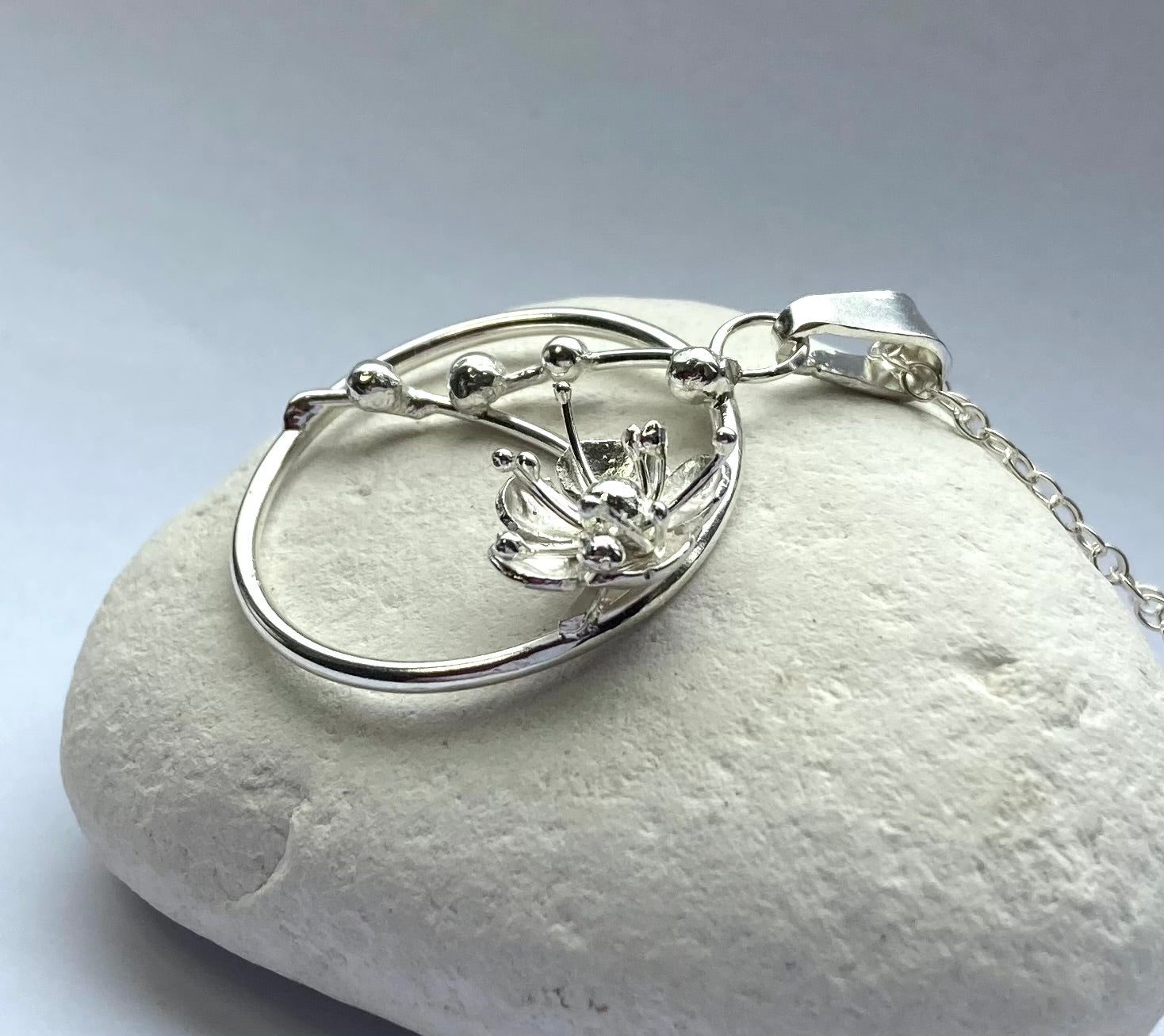 close up of cherry blossom hand forged circle pendant showing stamens, resting on white pebble