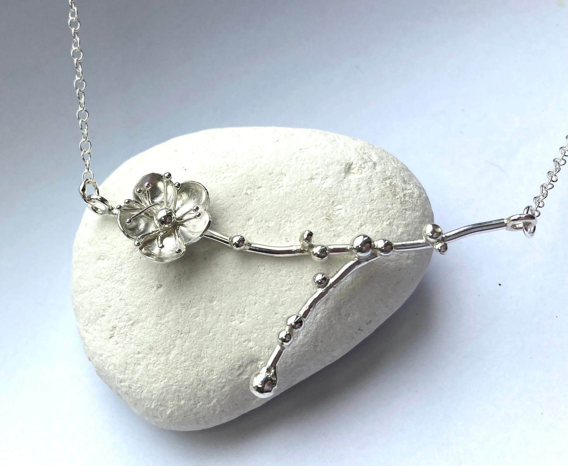 cherry blossom sprig silver necklace, on white pebble