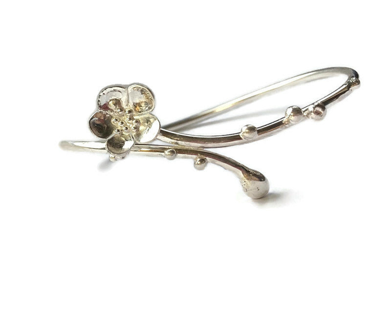 elegant curving silver bangle with single cherry blossom flower and buds, on white background