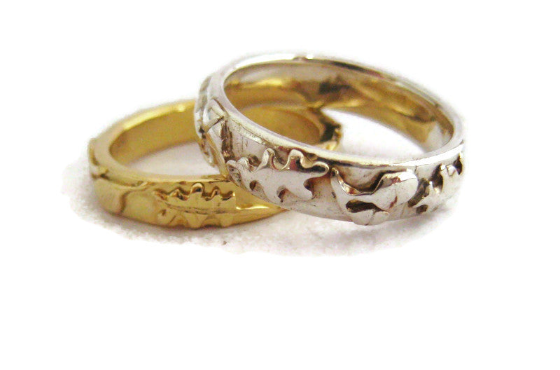 two rings, one yellow gold and one white gold  both with an oak and acorn pattern around the band, on a white background