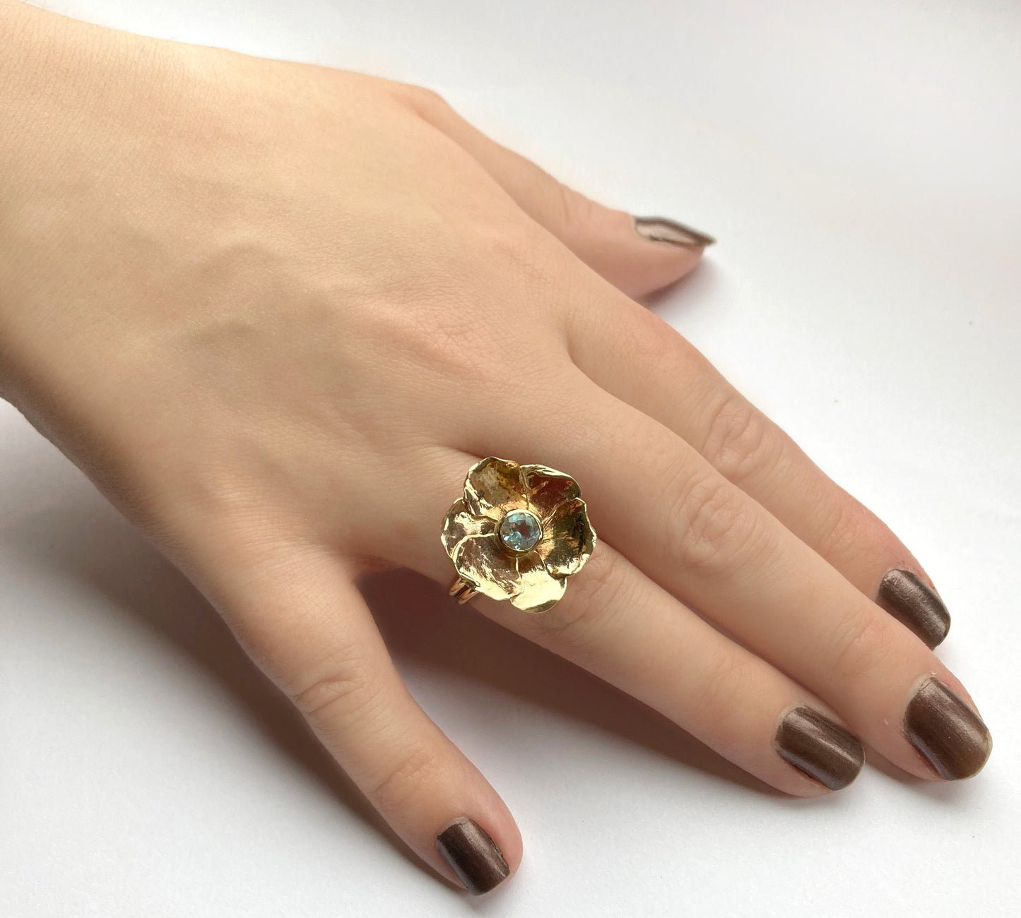 large gold flower ring with blue topaz, worn on hand
