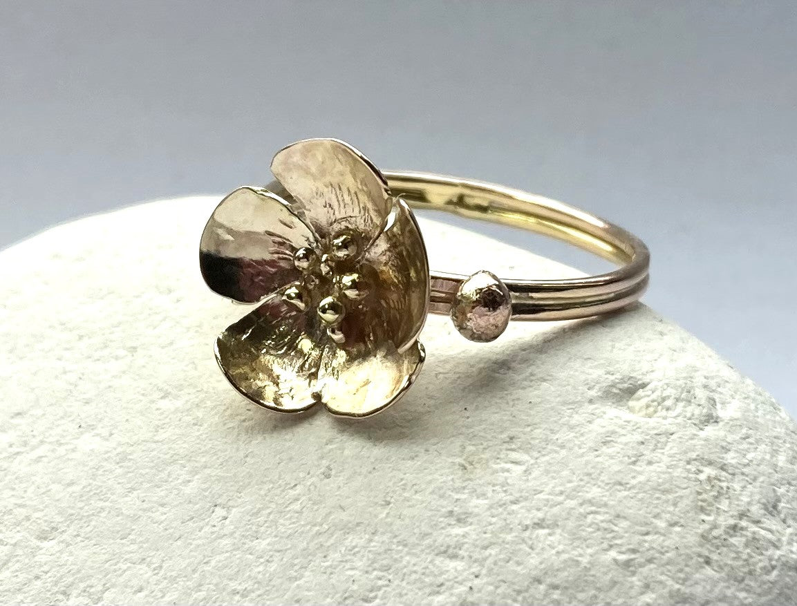 detailed view of gold flower ring with stamens, resting on white pebble