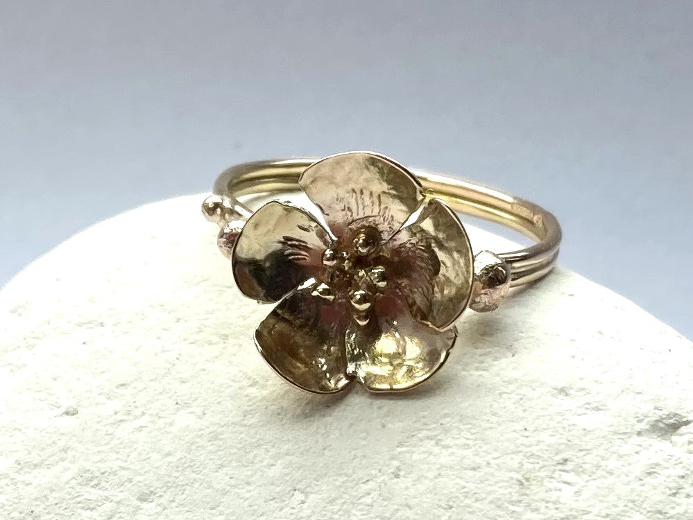front view of rose gold blossom ring, on white pebble