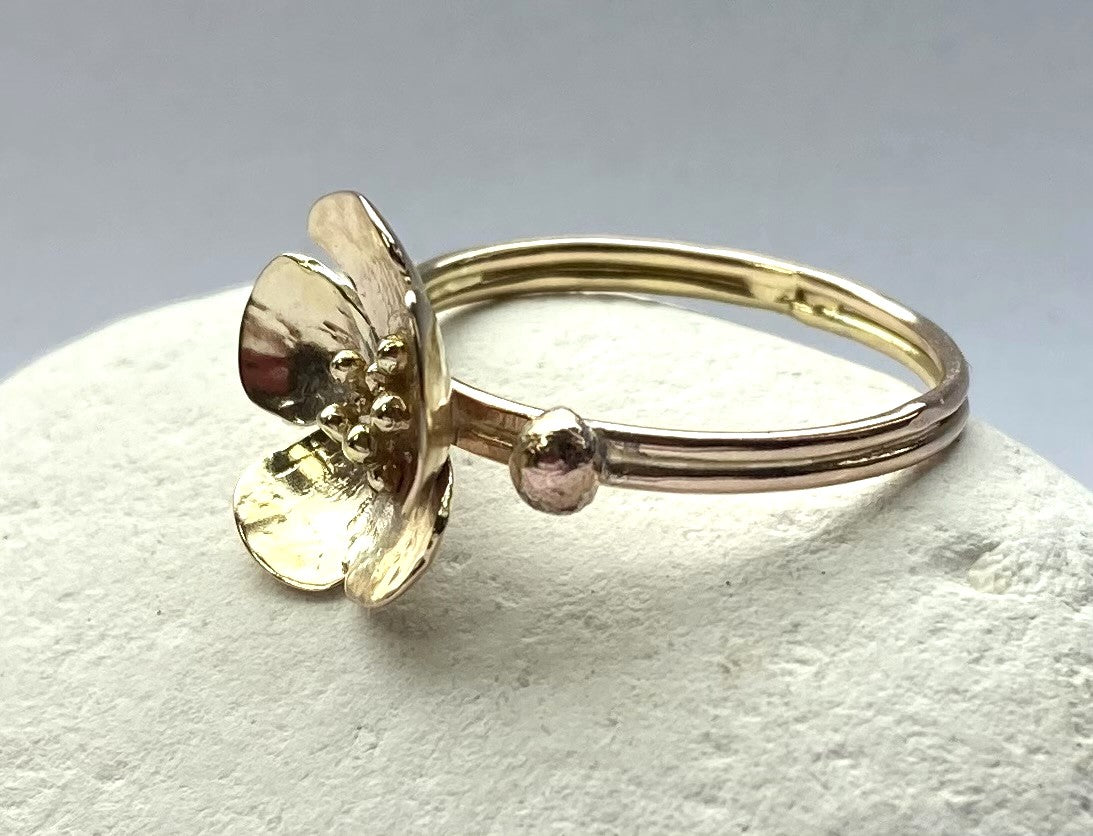 yellow gold dual shank flower ring, resting on white pebble