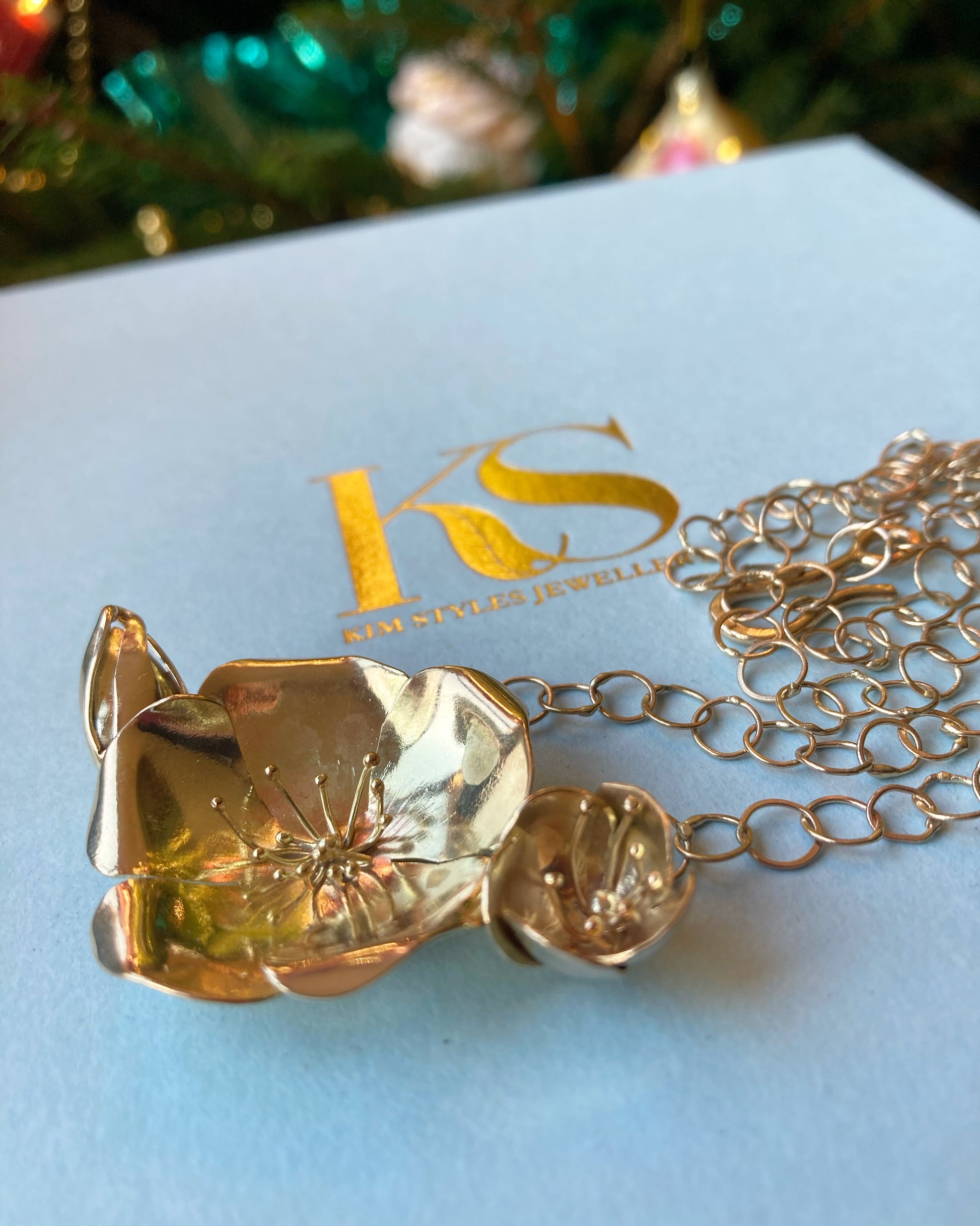 large gold flower necklace and chain on pale blue box printed with Kim-Styles-Jewellery logo in gold
