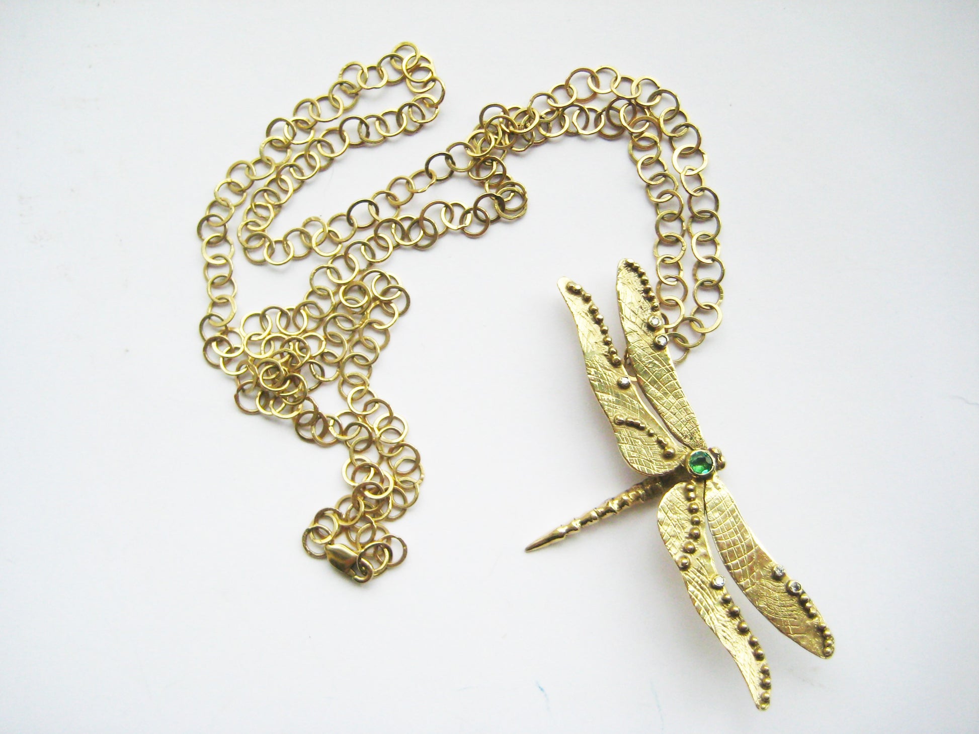 large link gold chain lying loosely with chunky yellow gold dragonfly pendant on white background