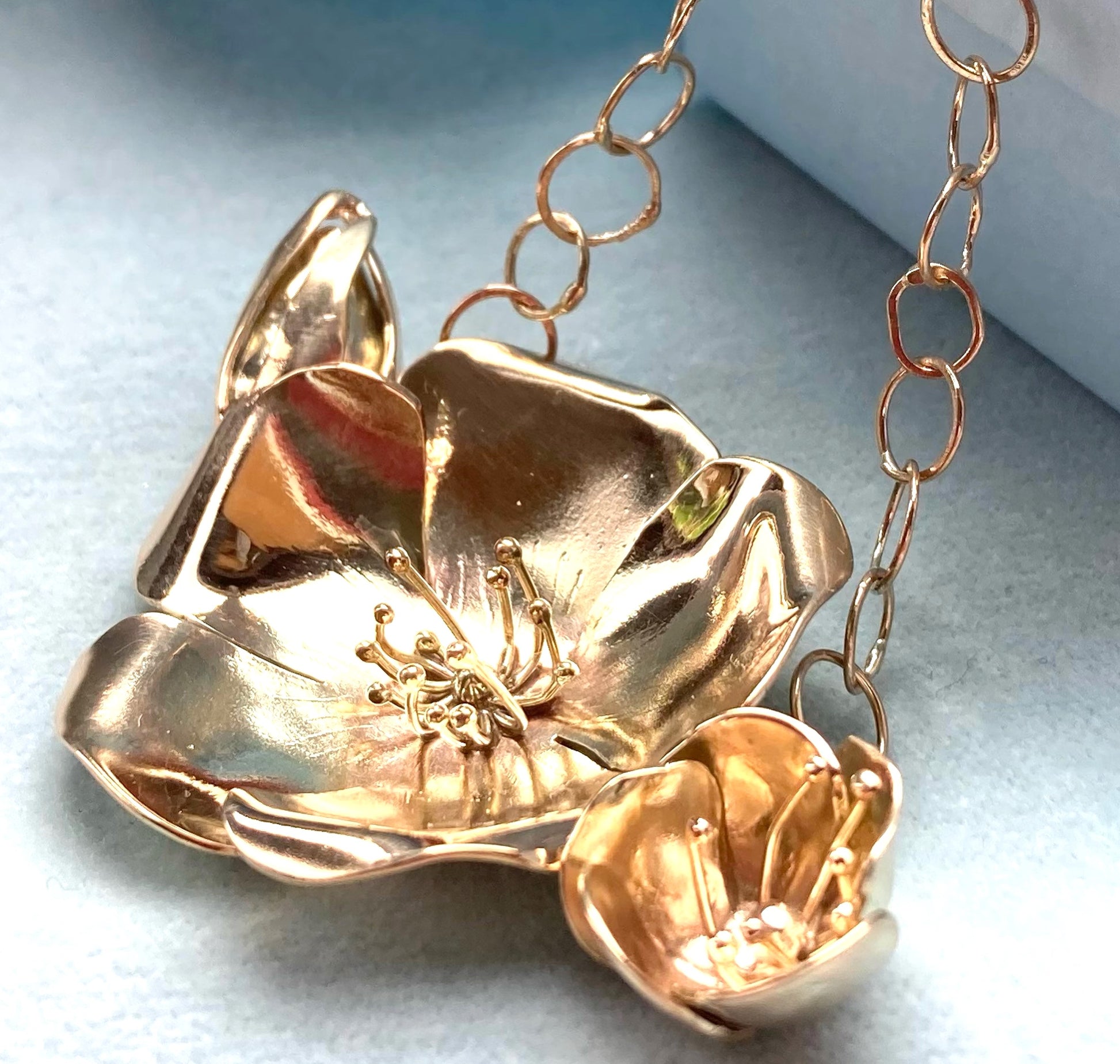 close up of detailed wild rose cluster yellow gold necklace and chain on pale blue background 