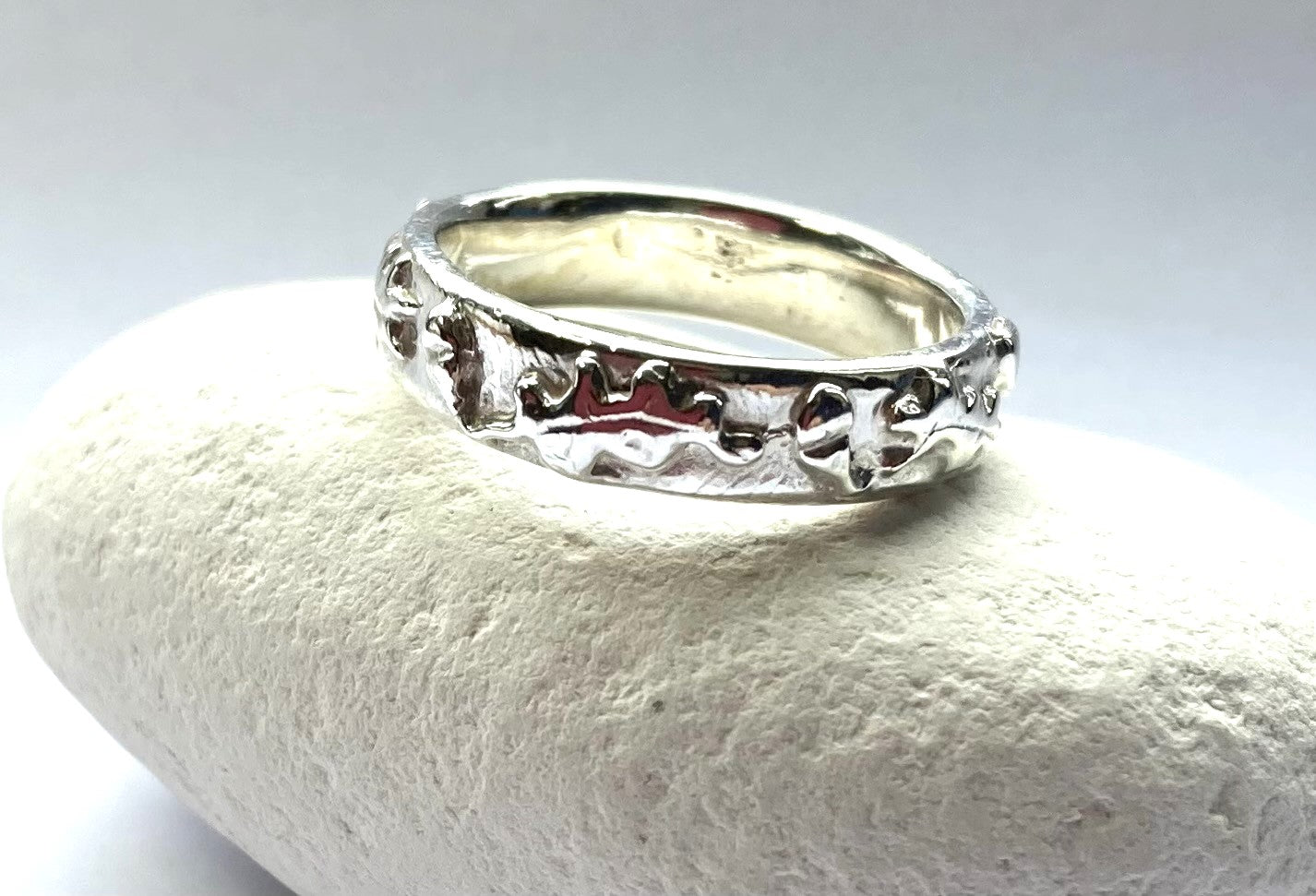 oak and acorn pattern wedding ring in white metal, resting on a white pebble
