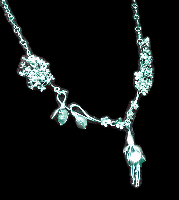 Handmade silver botanical necklace of various flowers including lilac, snowdrops, fuchsia, lily of the valley and forget-me-nots, on black background